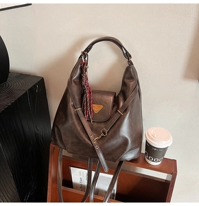 Macro shot of dark brown leather hobo bag with gold triangle plaque and plaid tassel