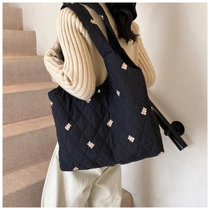 Detail view of large black quilted tote bag with cute bear embroidery and wide strap