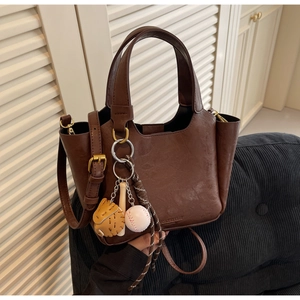 Détail du sac seau marron foncé avec breloques de baseball et cuir texturé de qualité