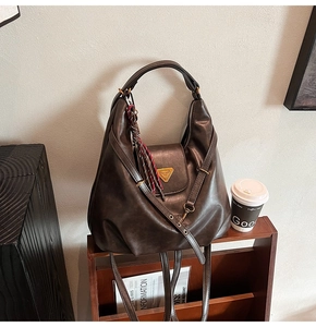 Detail of dark brown leather tote featuring metal triangle hardware and woven tassel
