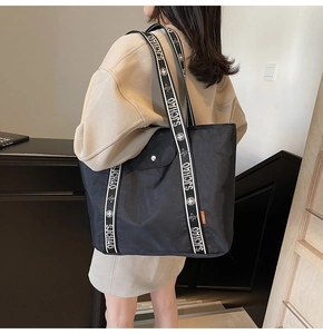 Detail of black tote bag shoulder straps featuring white letter branding and metal snap button