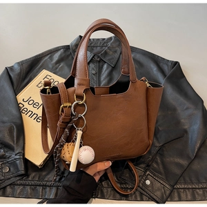 Détail d'un sac seau marron avec charm de baseball sur une veste en cuir noir