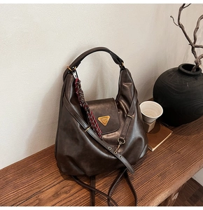Detail of dark brown leather hobo bag with gold hardware on a wooden table setup