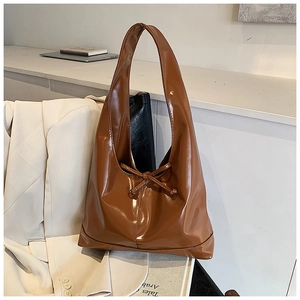 Detail of glossy caramel brown tote bag featuring a decorative bow on the smooth leather surface