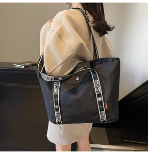 Detail of a large black tote bag featuring a branded webbing strap and magnetic leather flap