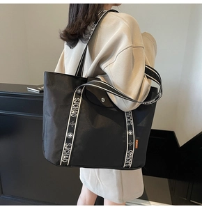 Detail of a black large-capacity tote bag with unique letter-printed shoulder straps
