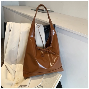 Close-up of a brown patent leather tote bag featuring a decorative bow on the front
