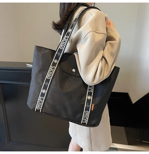 Side view of a large black canvas tote bag with decorative brand straps for daily commute