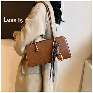 Detalle de bolso retro marrón oscuro con cinta azul y colgante de béisbol