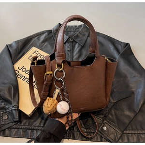 Détail d'un sac seau vintage marron avec breloques de baseball sur fond de veste en cuir