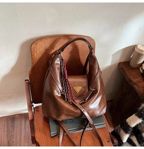 Brown vintage PU leather tote bag on wooden chair with woven tassel charm and metal logo
