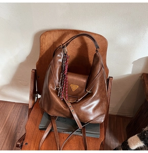 Close-up of vintage brown leather hobo bag with triangle logo and rope charm on chair