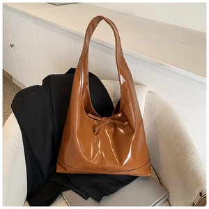 Close-up of brown patent leather tote bag featuring a decorative ribbon bow detail