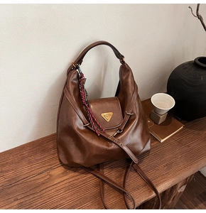 Detail of vintage brown leather hobo bag with gold triangle logo on wooden bench