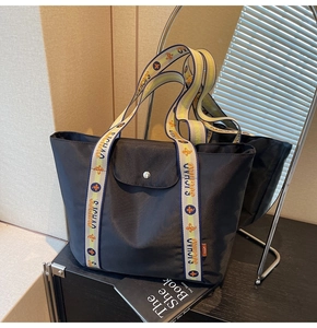 Detail of black nylon tote bag featuring floral woven strap and magnetic flap closure