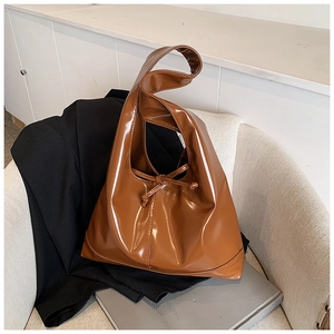 Close-up of a glossy dark brown tote bag with decorative knot on a beige chair