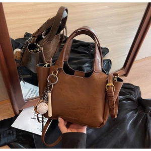 Détail du sac seau marron vintage montrant la texture cuir mat et le porte-clés créatif