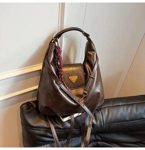 Detail of dark brown vintage hobo bag with glossy leather texture and woven rope charm