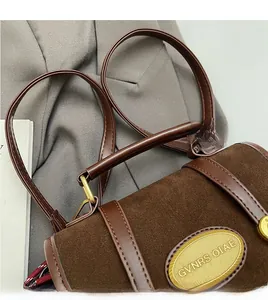 Détail du sac en daim marron avec poignée en cuir foncé et garnitures ovales dorées