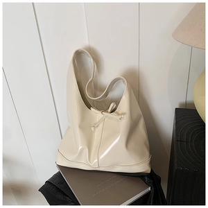 Detail of a creamy white high-gloss tote bag with drawstring on a dark wood table
