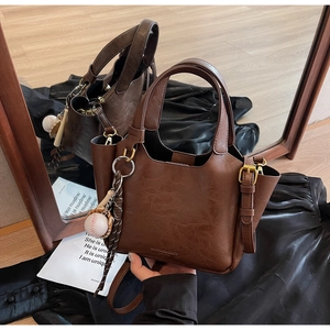 Détail du sac seau marron foncé avec ferrures dorées et breloque baseball sur soie