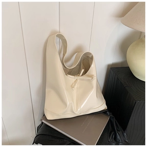 Detail shot of a glossy cream hobo bag with drawstring décor on black wooden stand