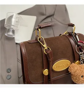 Détails du sac bandoulière vintage marron avec plaque logo dorée et breloque en ourson