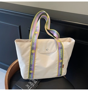 Detail of colorful woven handles with SJCHAO lettering on a cream tote bag