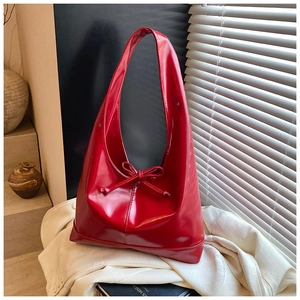 Detail of red Hobo tote bag with decorative bow placed on books in artistic light