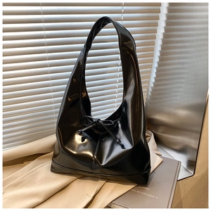 Detail of black glossy tote bag with bow drawstring on a trench coat background