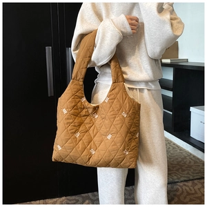 Detailed shot of brown quilted tote bag featuring white bear embroidery and wide strap