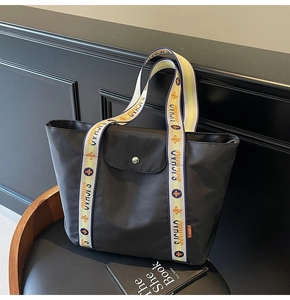 Close-up of black nylon tote bag with colorful embroidered straps and metal buckle