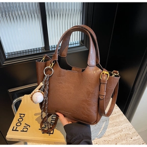 Détail du sac seau rétro marron foncé avec texture cuir et breloque de baseball