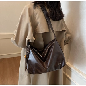 Detailed view of dark brown faux leather hobo bag with gold charm and metal logo