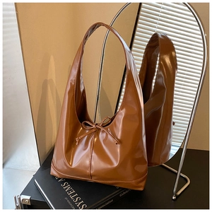 Detail of caramel brown glossy hobo bag with bow drawstring on a minimalist book