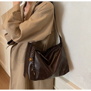 Detail of dark brown tote bag featuring leather texture and golden bell charm