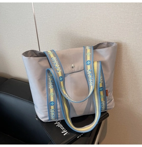 Close-up of a grey tote bag with colorful SUCHA0 embroidery on woven handles