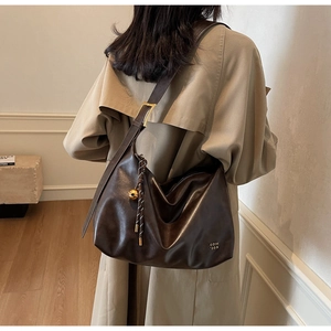 Detail of a dark brown leather hobo bag with gold buckle and decorative bell charm