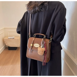 Detail of a brown leather crossbody bag featuring a cute plush bear pendant and metal logo