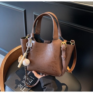 Détail du sac seau en cuir marron foncé avec grain litchi et breloque de baseball