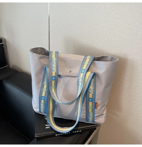 Close-up of light grey nylon tote bag with unique blue-yellow logo woven shoulder strap