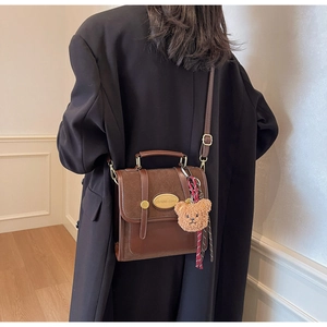 Close-up of vintage brown crossbody bag with matte flap and cute plush bear charm accessory