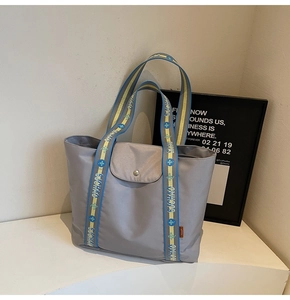 Close-up of gray tote bag featuring branded contrast webbing straps and metal snap button
