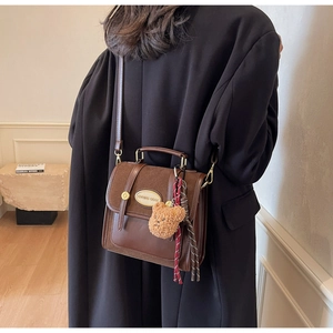 Detail of vintage coffee crossbody bag with matte flap and fuzzy bear keychain accessory