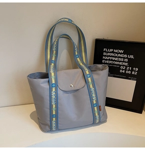 Detail of grey nylon tote bag featuring blue and yellow jacquard handles and magnetic flap