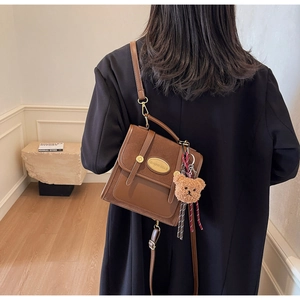 Détail d'un sac bandoulière marron avec patchwork bimatière et un charme d'ours en peluche