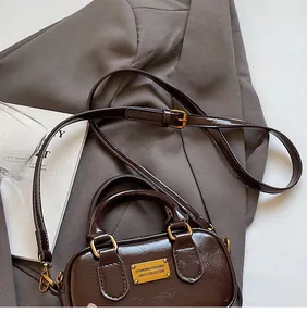 Detailed close-up of dark brown glossy leather handbag with gold metal logo and strap