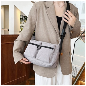 Detail of grey nylon crossbody bag with dual zipper pockets on neutral suit outfit