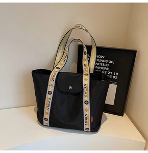 Detail of the woven shoulder strap featuring orange floral patterns on a black tote bag