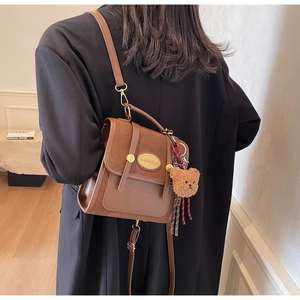 Détail du sac à bandoulière marron vintage avec logo en métal et breloque ours en peluche